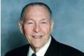 Elderly man smiling in a suit against a gray background.