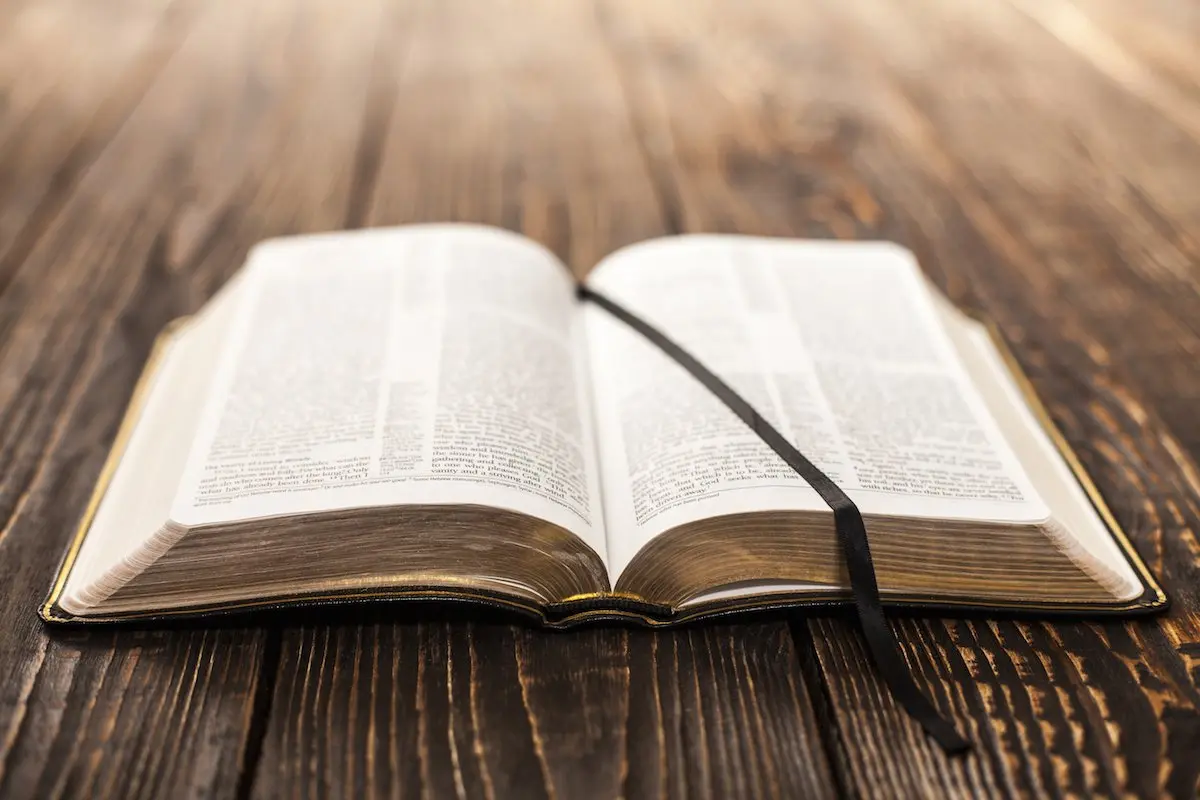 Open Bible on a wooden table with a black ribbon bookmark.