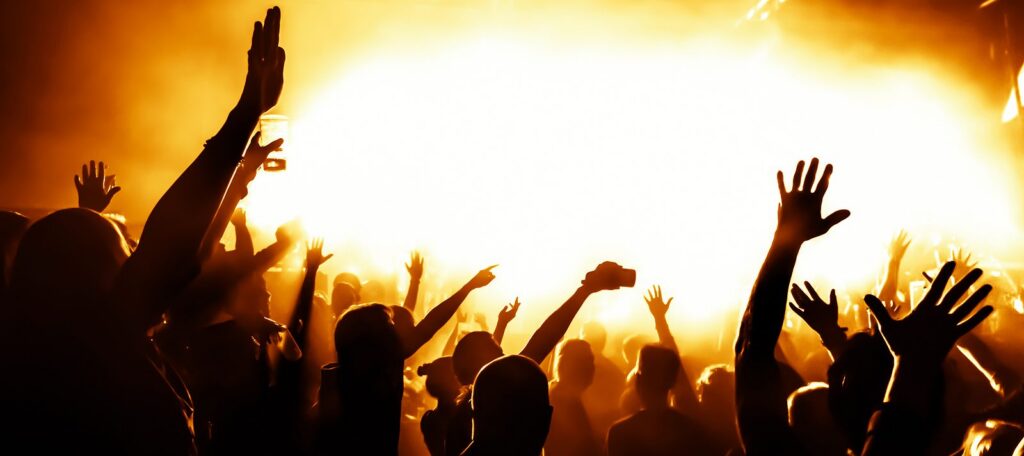 Silhouetted crowd with raised hands at a brightly lit concert.