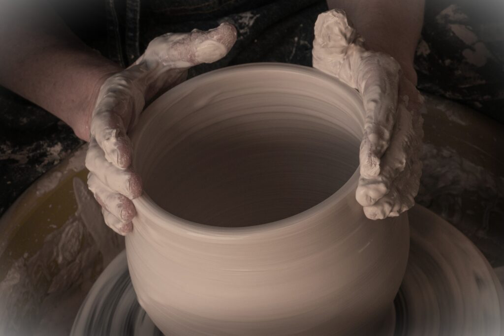 Hands shaping a clay pot on a pottery wheel, covered in wet clay.