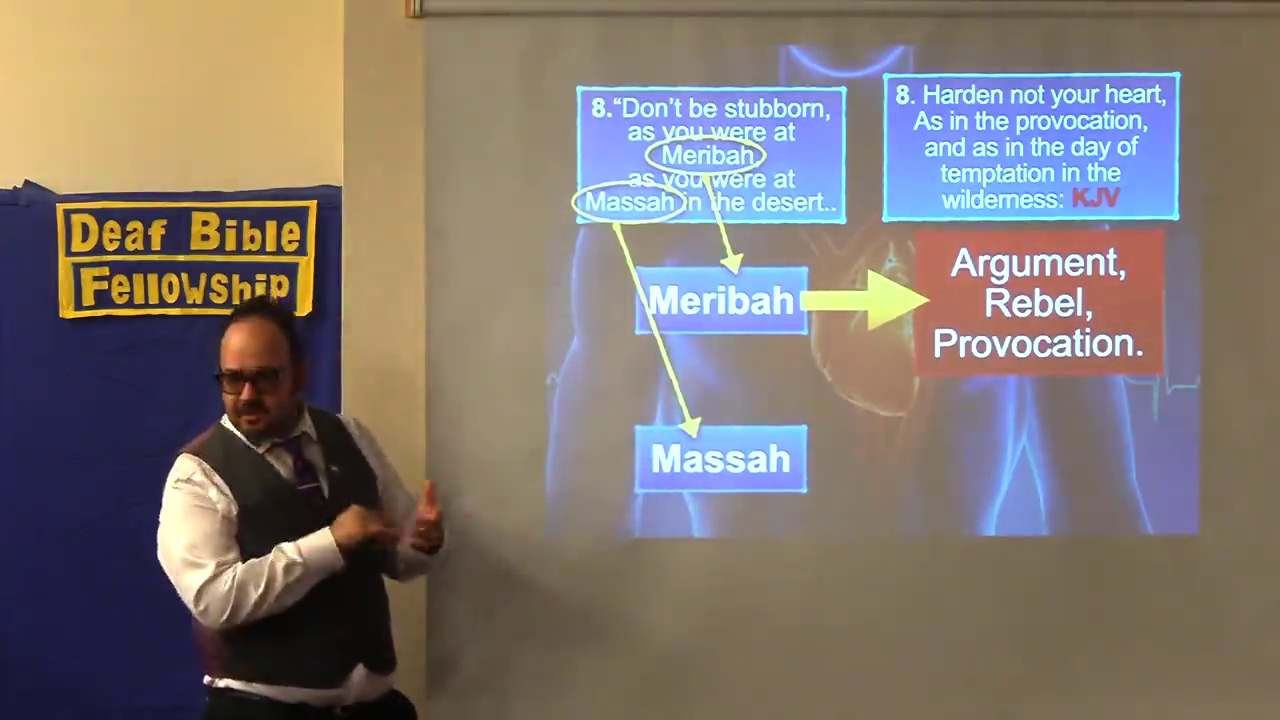 Man gestures near a presentation on Meribah and Massah at Deaf Bible Fellowship.
